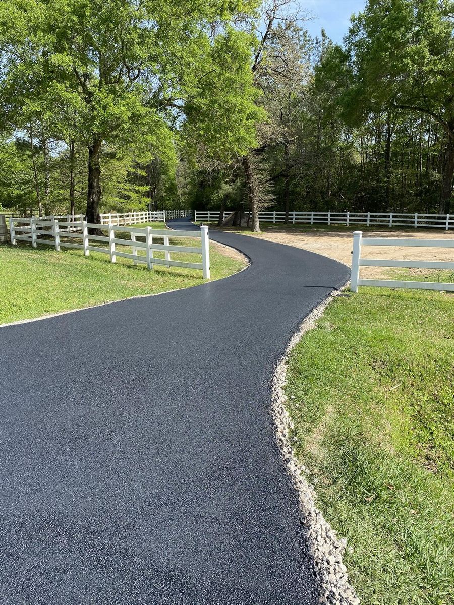 Winding residential asphalt driveway along a white fence